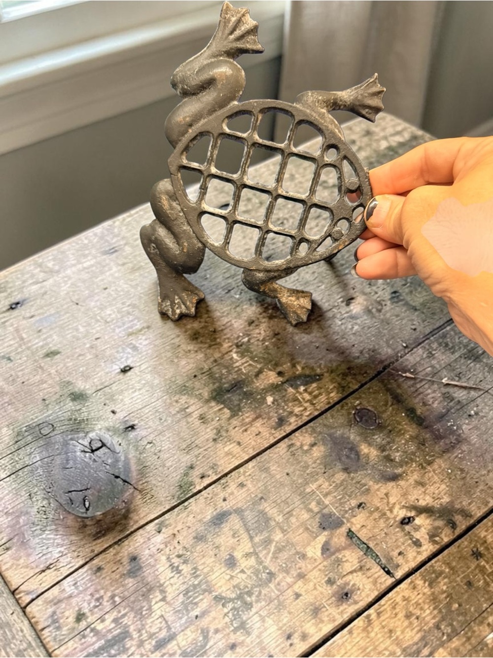 A vintage cast iron frog trivet with a grid pattern.